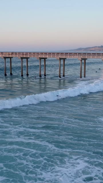 Low aerial view of the beach, the surf and the pier at Black’s Beach.