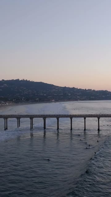 Low aerial view of the beach, the surf and the pier at Black’s Beach, with surfers out.