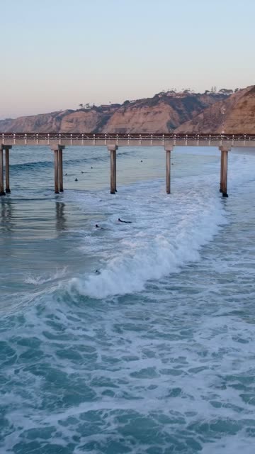 Low aerial view of the beach, the surf and the pier at Black’s Beach, with surfers out.