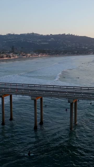 Aerial view of the beach, the surf and the pier at Black’s Beach, with surfers out.