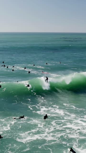 Low aerial view of the beach, the surf and the ocean at Swamis, with surfers out.