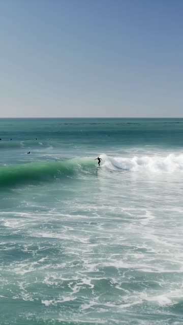 Low aerial view of the beach, the surf and the ocean at Swamis, with surfers out.