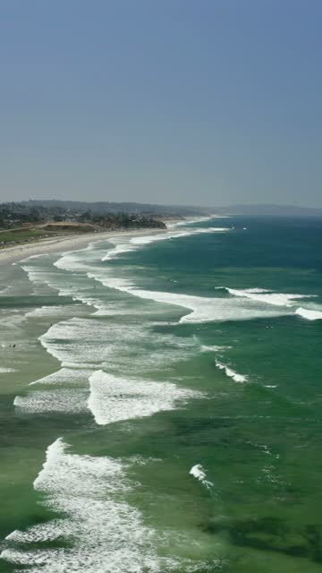Aerial view of the beach, the surf and the ocean in Cardiff, with surfers out.