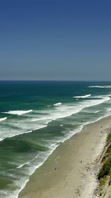 Aerial view of the beach, the surf and the ocean in Cardiff, with people walking.