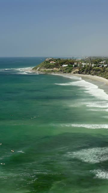 Aerial view of the beach, the surf and the ocean in Cardiff, with surfers out.