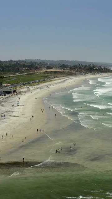 Aerial view of the beach, the surf and the ocean in Cardiff, with people walking.