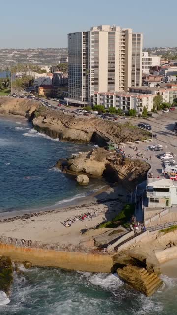 Aerial view of the cliffs, the ocean and the buildings at La Jolla Cove, with people walking.