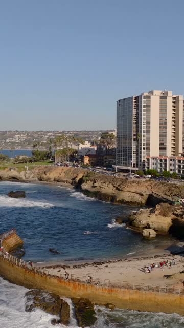 Aerial view of the cliffs, the surf and palm trees at La Jolla Cove, with people walking.