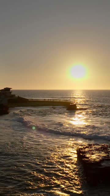 Low aerial view of the cliffs, the surf and the ocean at La Jolla Cove, with people walking.