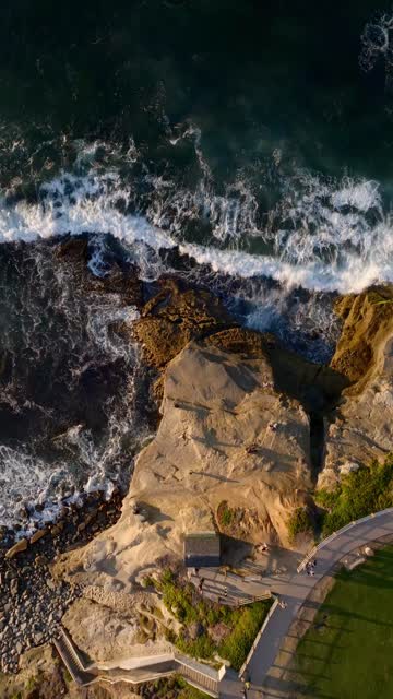 Aerial view of the cliffs, the surf and the ocean at La Jolla Cove, with people walking.