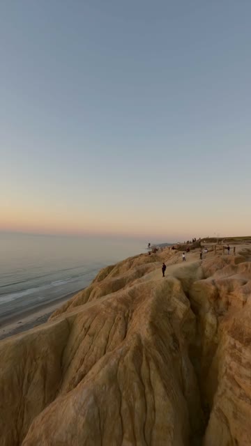 Low aerial view of the cliffs, the ocean and the beach at Black’s Beach, with people walking.