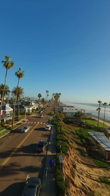 Low aerial view of a residential street, palm trees and the ocean in Oceanside, with people walking.