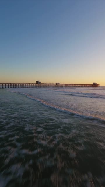 Low aerial view of the beach, the surf and the pier in Oceanside.