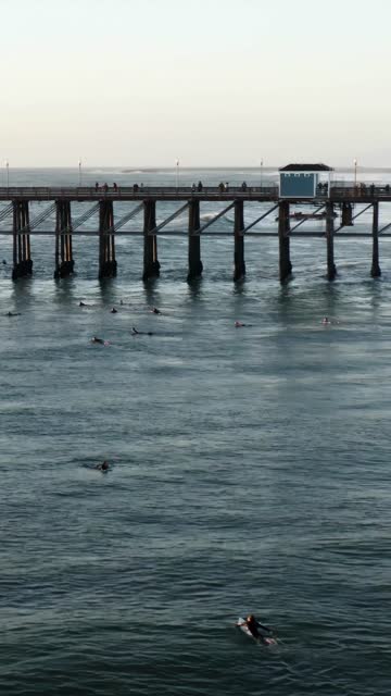Low aerial view of the beach, the surf and the pier in Oceanside, with surfers out.