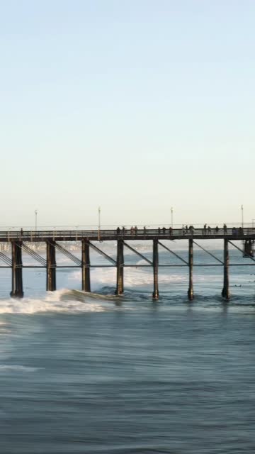 The beach, the surf and the pier in Oceanside, with people walking.