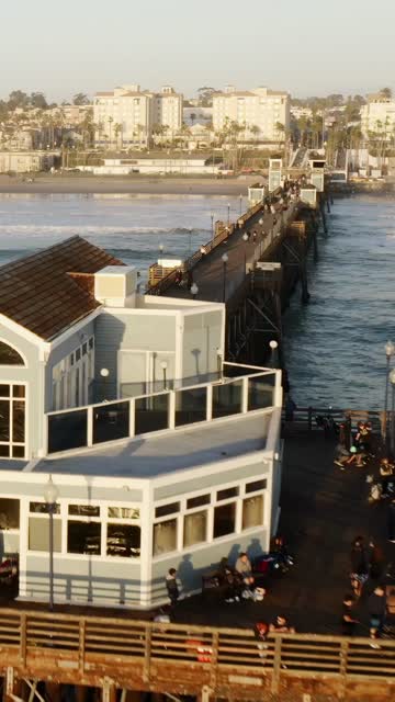 Low aerial view of the beach, the surf and the pier in Oceanside, with people walking.