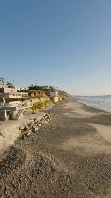Low aerial view of the beach, the surf and palm trees at Moonlight Beach, with people walking.