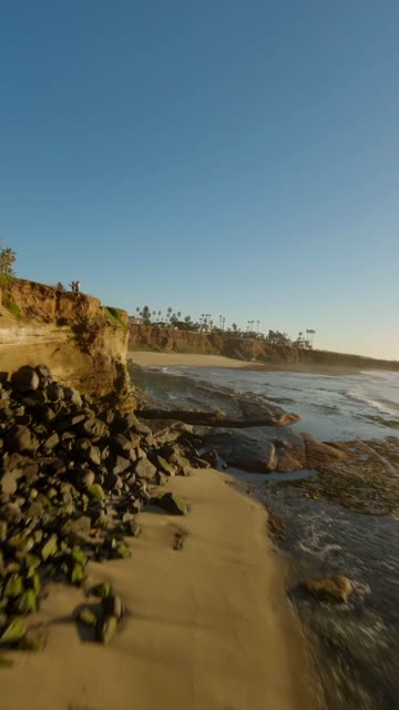 Low aerial view of the cliffs, the surf and palm trees at Sunset Cliffs, with people walking.