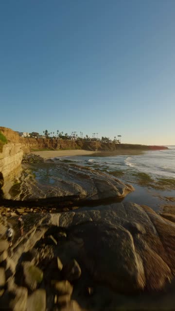 Low aerial view of the cliffs, the surf and palm trees at Sunset Cliffs.