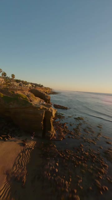 Low aerial view of the cliffs, the surf and palm trees at Sunset Cliffs, with people walking.