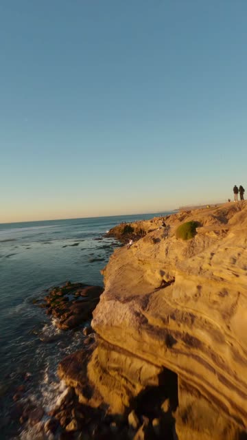 Low aerial view of the cliffs, the ocean and open country at Sunset Cliffs, with people walking.