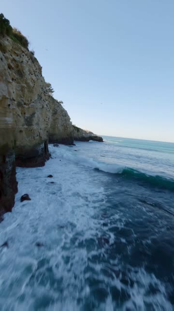 Low aerial view of the cliffs, the surf and the ocean at Coast Walk Trail.