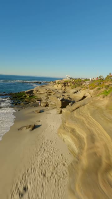 Low aerial view of the cliffs, the surf and the ocean at La Jolla Cove.