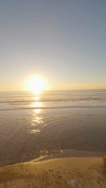 Low aerial view of the beach, the surf and the ocean at Moonlight Beach, with people walking.