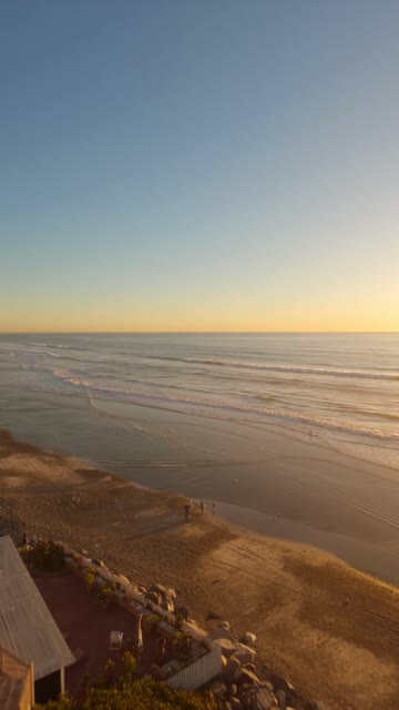 Aerial view of the beach, the surf and the ocean at Moonlight Beach, with people walking.