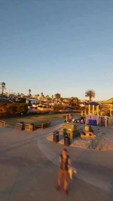 Low aerial view of a park, palm trees and homes at Moonlight Beach, with people walking.