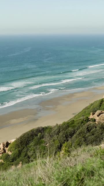 Elevated view of the cliffs, the surf and the ocean at Black’s Beach, with people walking.