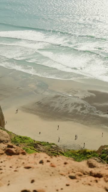 Elevated view of the cliffs, the surf and the ocean at Black’s Beach, with people walking.
