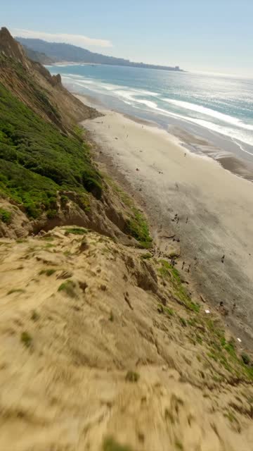 Aerial view of the cliffs, the surf and the ocean at Black’s Beach, with people walking.