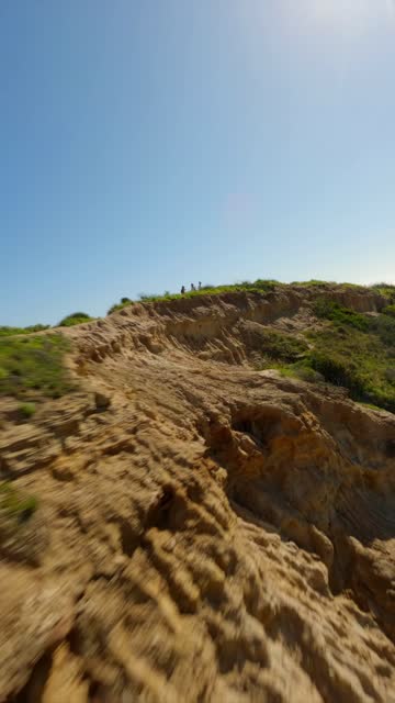 Low aerial view of the cliffs and open country at Black’s Beach, with people walking.
