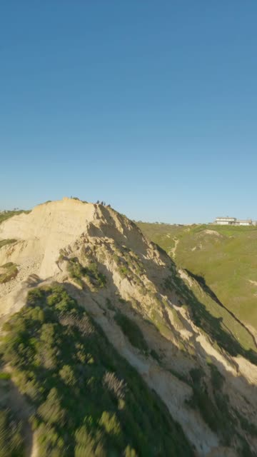 Low aerial view of the cliffs and open country at Black’s Beach, with people walking.