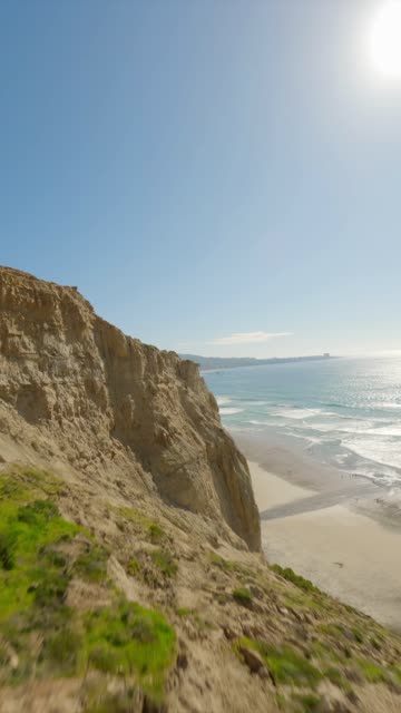 Low aerial view of the cliffs, the surf and the ocean at Black’s Beach.