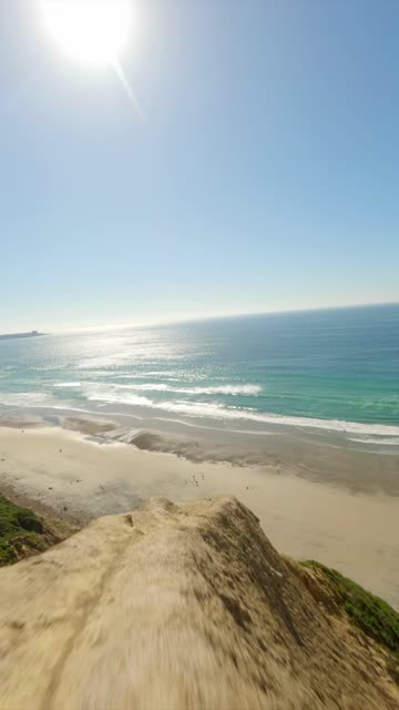 Aerial view of the cliffs, the surf and the ocean at Black’s Beach, with people walking.