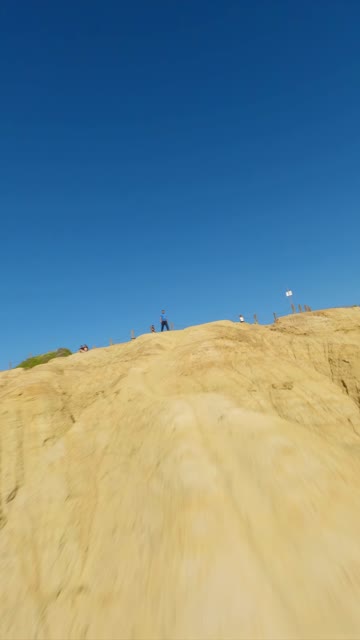 Low aerial view of the cliffs and open country at Black’s Beach, with people walking.