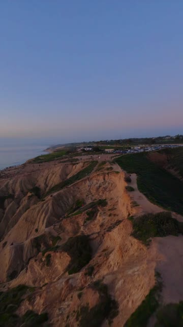 Aerial view of the cliffs, the ocean and open country at Black’s Beach, with people walking.