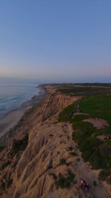 Aerial view of the cliffs, the ocean and the beach at Black’s Beach, with people walking.