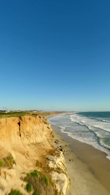 Low aerial view of the cliffs, the surf and the ocean in Carlsbad.