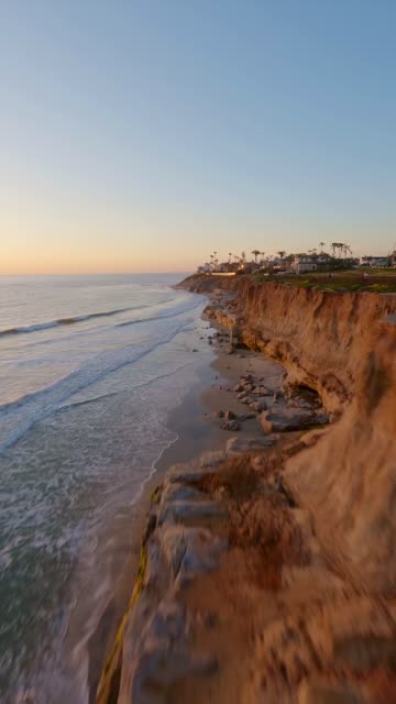Low aerial view of the cliffs, the surf and palm trees in Carlsbad.
