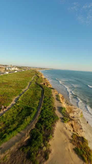 Aerial view of the cliffs, the surf and the ocean in Carlsbad, with people walking.