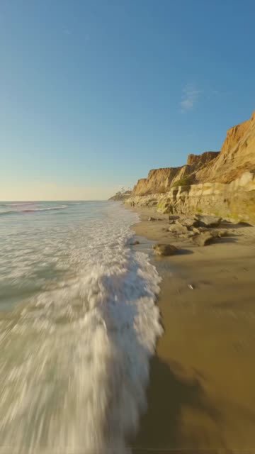 Low aerial view of the cliffs, the surf and the ocean in Carlsbad.