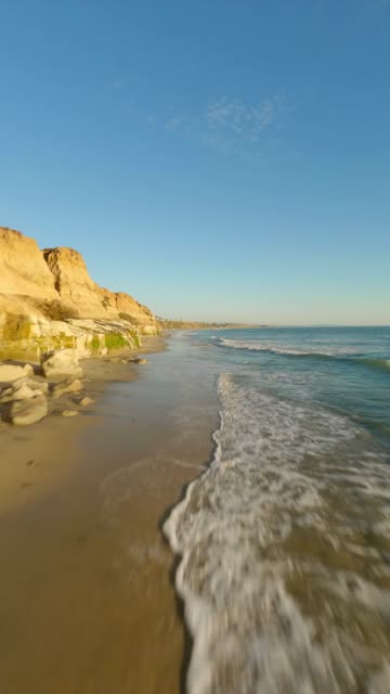 Low aerial view of the beach, the surf and the ocean in Carlsbad.