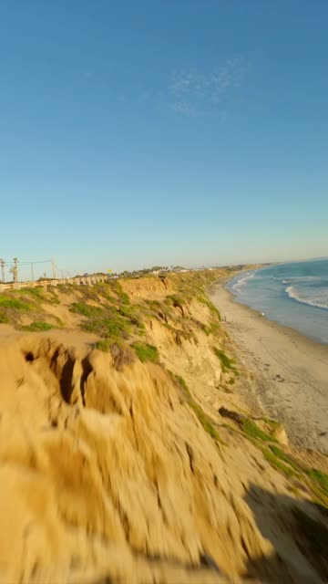 Low aerial view of the cliffs, the surf and the ocean in Carlsbad, with people walking.