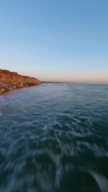 Low aerial view of the cliffs, the surf and the ocean in Carlsbad.