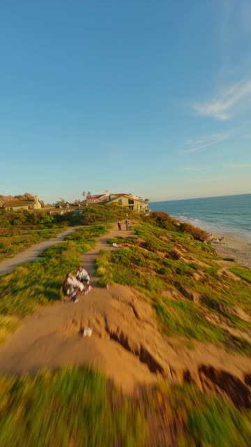 Low aerial view of the cliffs, the ocean and homes in Carlsbad, with people walking.
