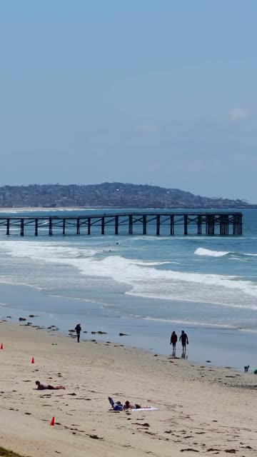 The beach, the surf and the pier in Pacific Beach, with people walking.