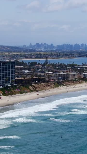 Aerial view of the beach, the surf and the skyline in Pacific Beach, with surfers out.